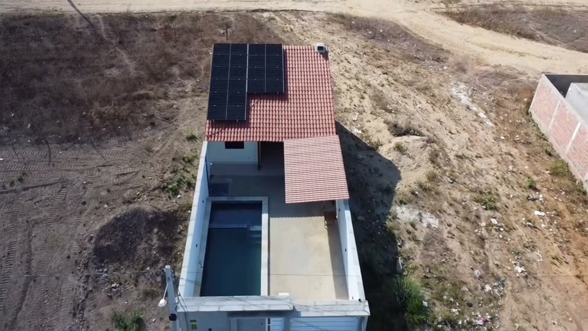 Vista de drone de casa com piscina em São José do Egito, com módulos solares escuros sobre o telhado de telha cerâmica e terreno de caatinga ao redor